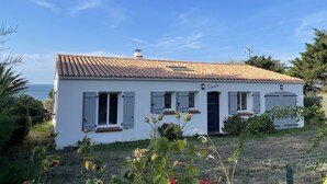 A white building with a tiled roof, a small porch, and a view of the sea. - Rare! Seafront vacation home with direct access to sea and beach (Pornic)
