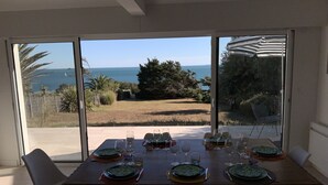 A dining table set for six with a view of the sea through large glass doors. - Rare! Seafront vacation home with direct access to sea and beach (Pornic)
