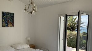 A bedroom with a bed, a chandelier, a nightstand, a lamp, a painting, and a sliding glass door leading to an outdoor area with a view of the sea. - Rare! Seafront vacation home with direct access to sea and beach (Pornic)