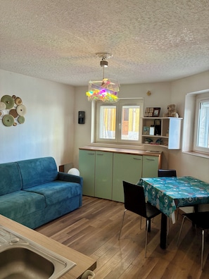 Un espacio habitable compacto con kitchenette, un área de comedor con mesa y sillas, un sofá y una lámpara en el techo.