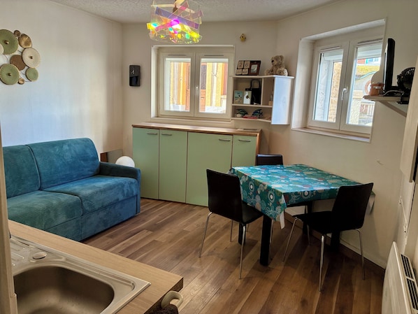 Un espacio habitable compacto con sofá, una mesa de comedor, una zona de cocina y una ventana.