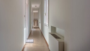 A narrow hallway with a radiator, a door at the end, and a window on the right wall.