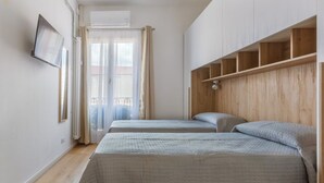 A bedroom with two beds, a TV, a wooden headboard, and a window with curtains.