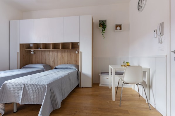 A bedroom with two beds, a desk, a chair, a small plant, and a clock on the wall.
