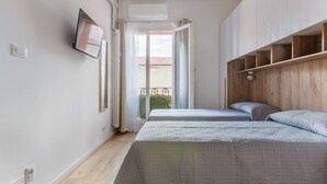 A bedroom with two beds, a TV, a balcony, and a wooden shelf unit.