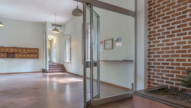 A spacious lobby with a glass door entrance, a brick wall, a wooden bench, and a tiled floor.