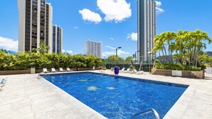 A swimming pool with lounge chairs, surrounded by palm trees and tall buildings. - Ocean view, Newly Renovated Luxury Waikiki Hotel, Free Parking. (Honolulu)
