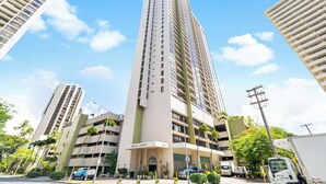 A high-rise building with multiple floors, a sign reading 'WAIKIKI SUNSET,' and several parked vehicles. - Ocean view, Newly Renovated Luxury Waikiki Hotel, Free Parking. (Honolulu)
