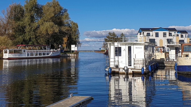 A river with a boat docked on the left and a small building with a sign 'RECHLIN' on the right.