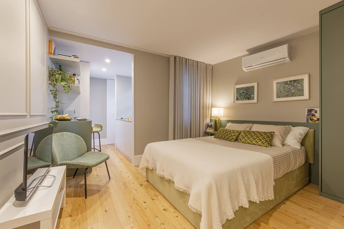 A bedroom with a bed, a desk, a chair, and a shelf with plants.
