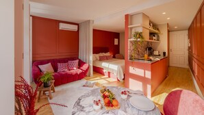 Una camera d'albergo moderna con arredamento nei toni del rosso e del bianco, un'area salotto accogliente, un angolo ristoro con tavolo in marmo e una piccola cucina attrezzata.