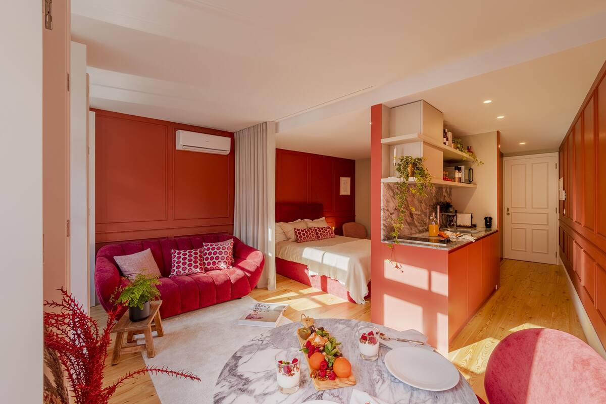 A modern hotel room with a red and white color scheme, a cozy seating area, a dining space with a marble table, and a kitchenette.