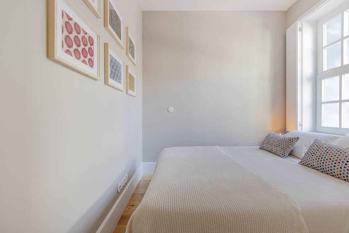 A bedroom with a large bed, a window, and framed artwork on the wall.