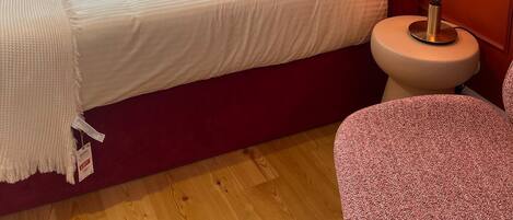 A bedroom with a red headboard, a bed with white and pink bedding, a bedside lamp, and a wooden floor.