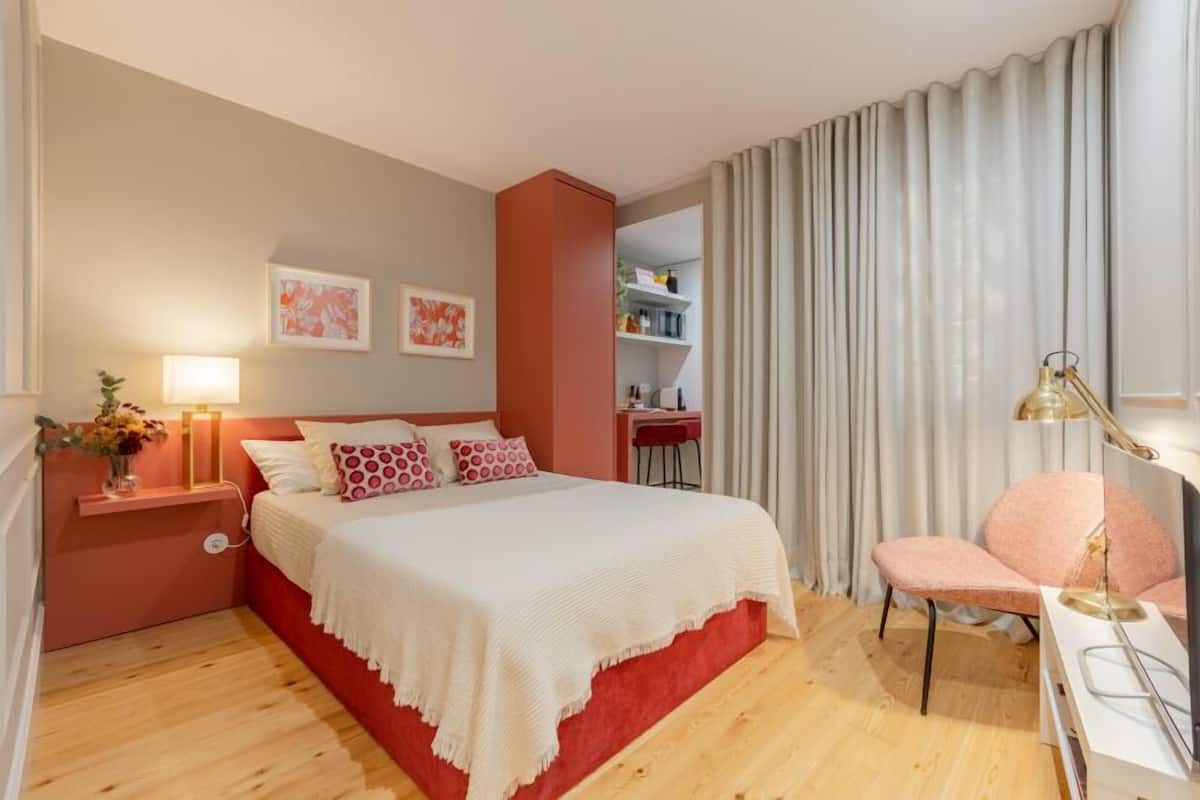 A bedroom with a bed, bedside table, lamp, chair, and a desk area.
