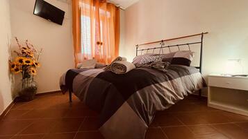 Un letto rifatto con una coperta a righe, un comodino con una lampada e un vaso con fiori.