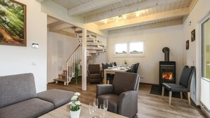 A cozy living room with a staircase, a dining area, and a wood-burning stove. - Ferienhausdorf Thale (Thale)
