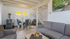 Una sala de estar moderna con un sofá gris, un comedor con mesa y sillas, una escalera y un cuadro de una cascada en la pared.