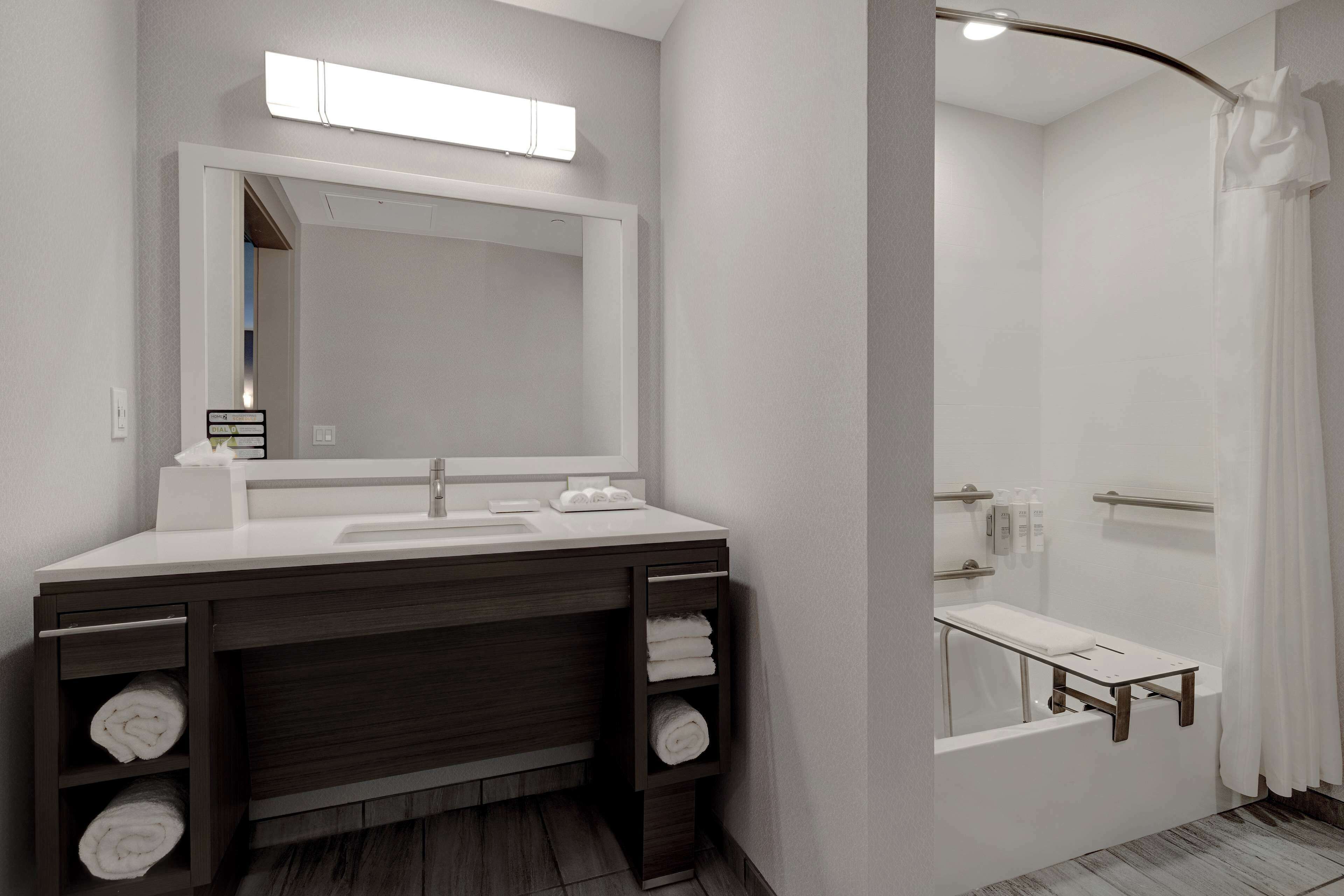 A modern bathroom with a large mirror, white sink, dark wooden vanity, and a shower area.