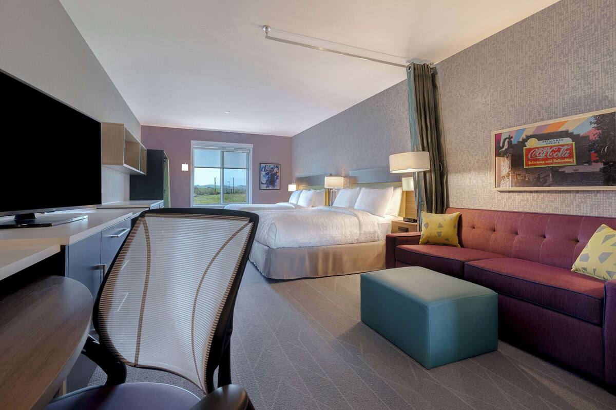 A hotel room with a bed, a sofa, a desk with a computer, a chair, and a television.
