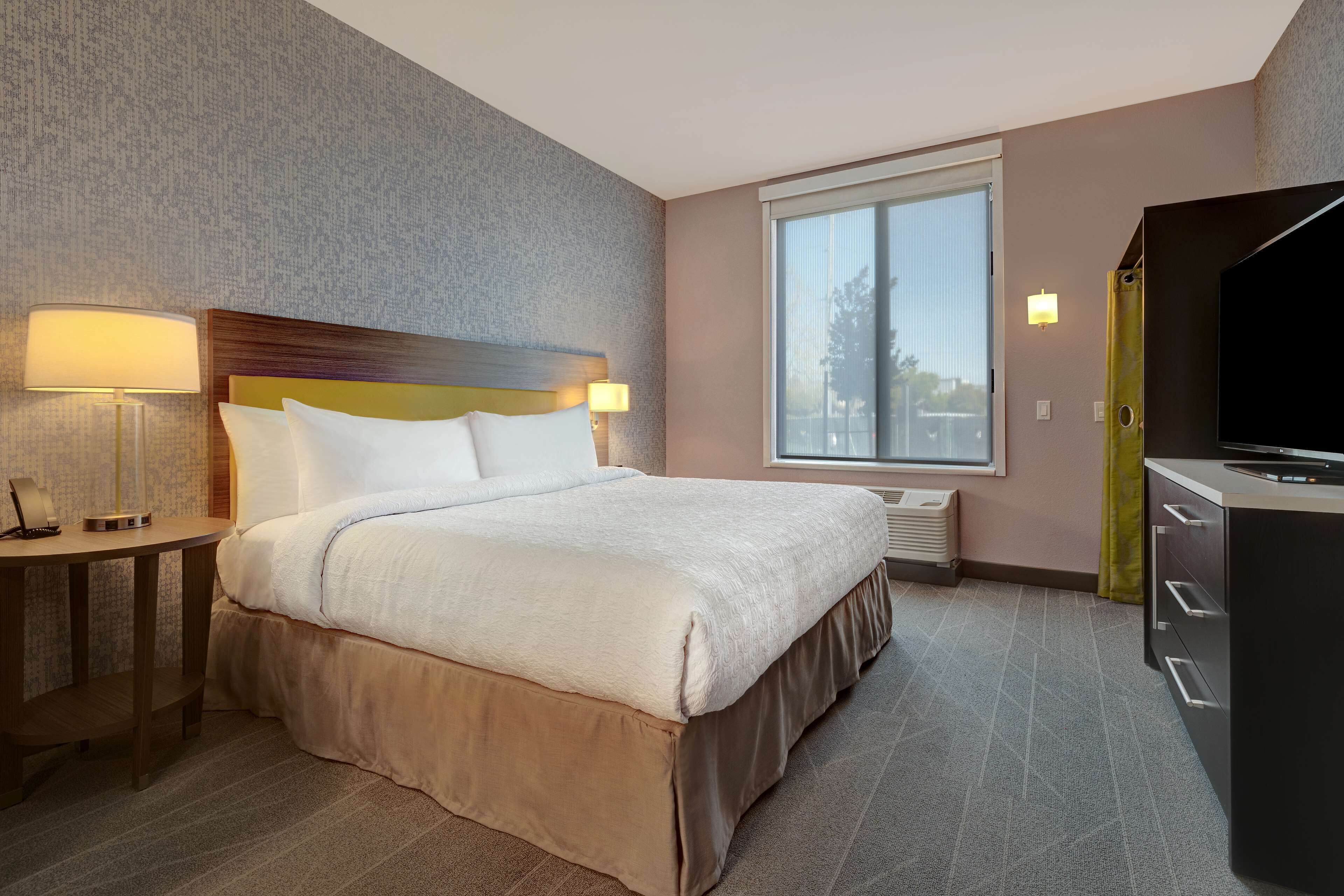 A hotel room with a bed, bedside lamps, a TV, and a window.