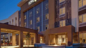 A hotel exterior with a sign reading "HOME 2" and a covered outdoor seating area with fire pits.