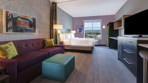 A hotel room with a sofa, a bed, a television, and a window with a view.