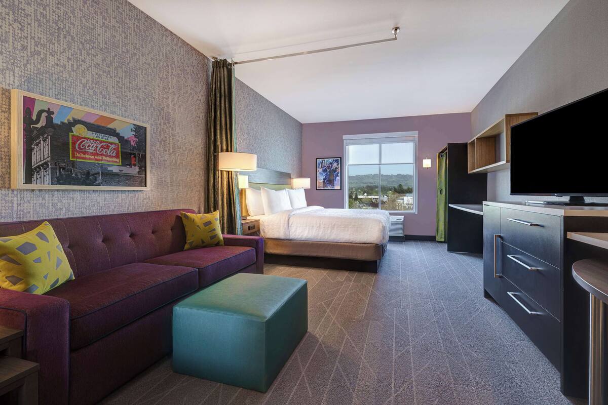 A hotel room with a sofa, a bed, a television, and a window with a view.