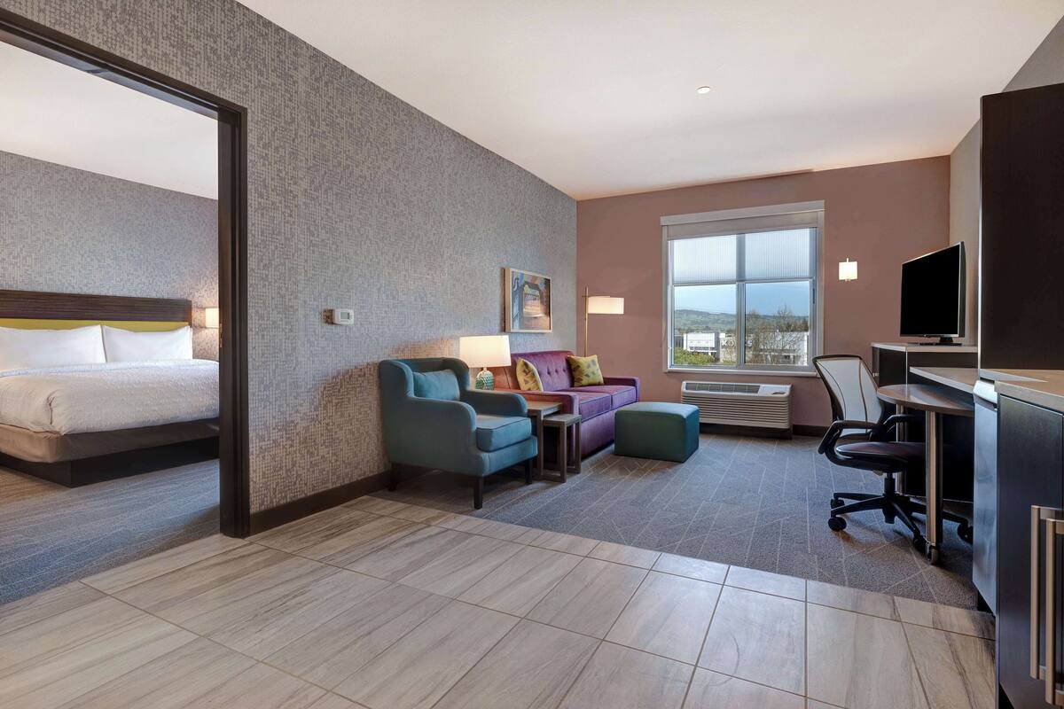 A hotel room with a bed, a sofa, a desk, and a TV.