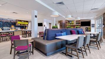 A modern restaurant with a central seating area, a kitchen in the background, and a TV mounted on the wall.