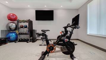 A home gym with exercise equipment, including a stationary bike, a TV, and various fitness balls.