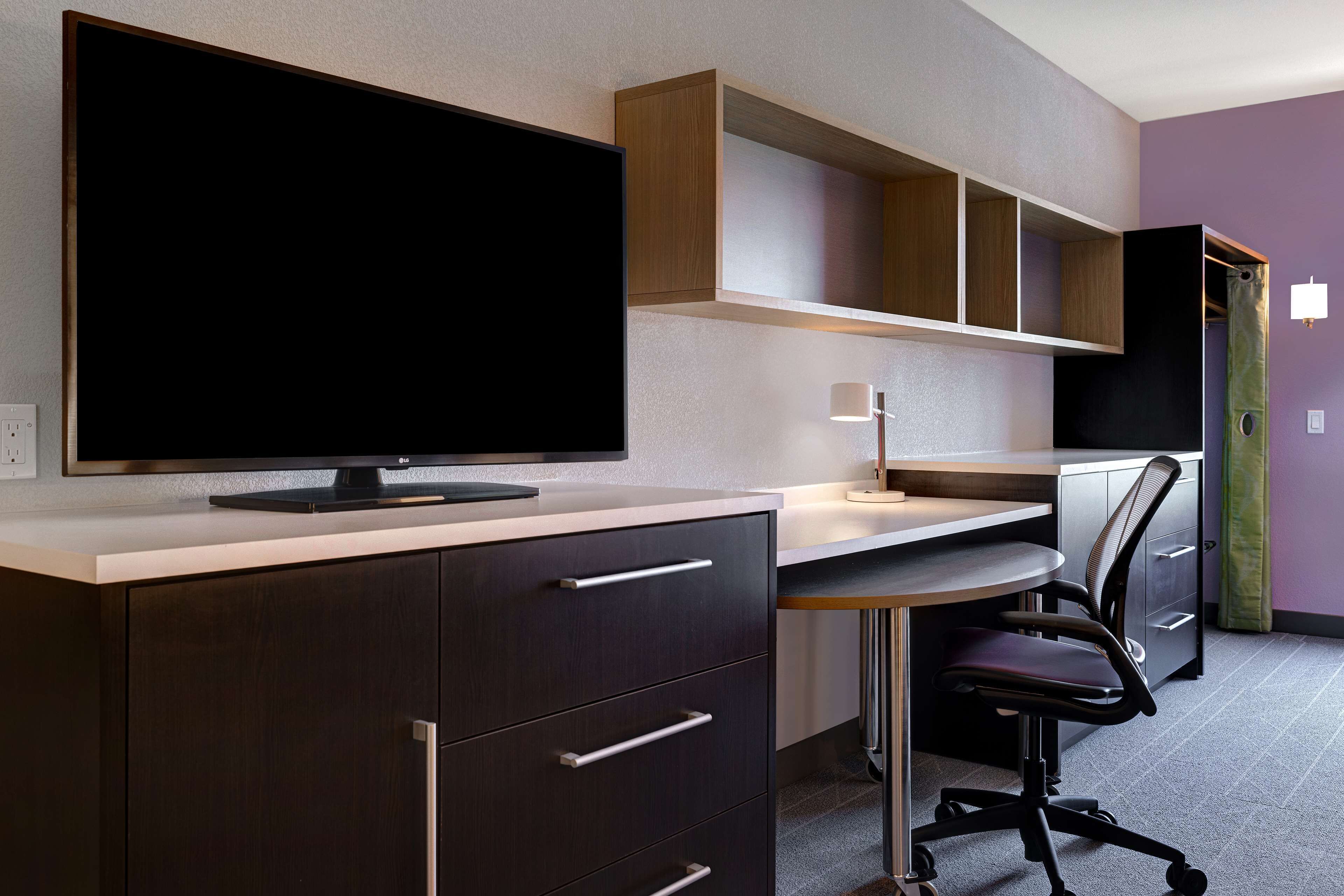 Un espacio de oficina moderno con televisor de pantalla plana, escritorio, silla y estanterías integradas.