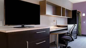 Un espacio de oficina moderno con televisor de pantalla plana, escritorio, silla y estanterías integradas.