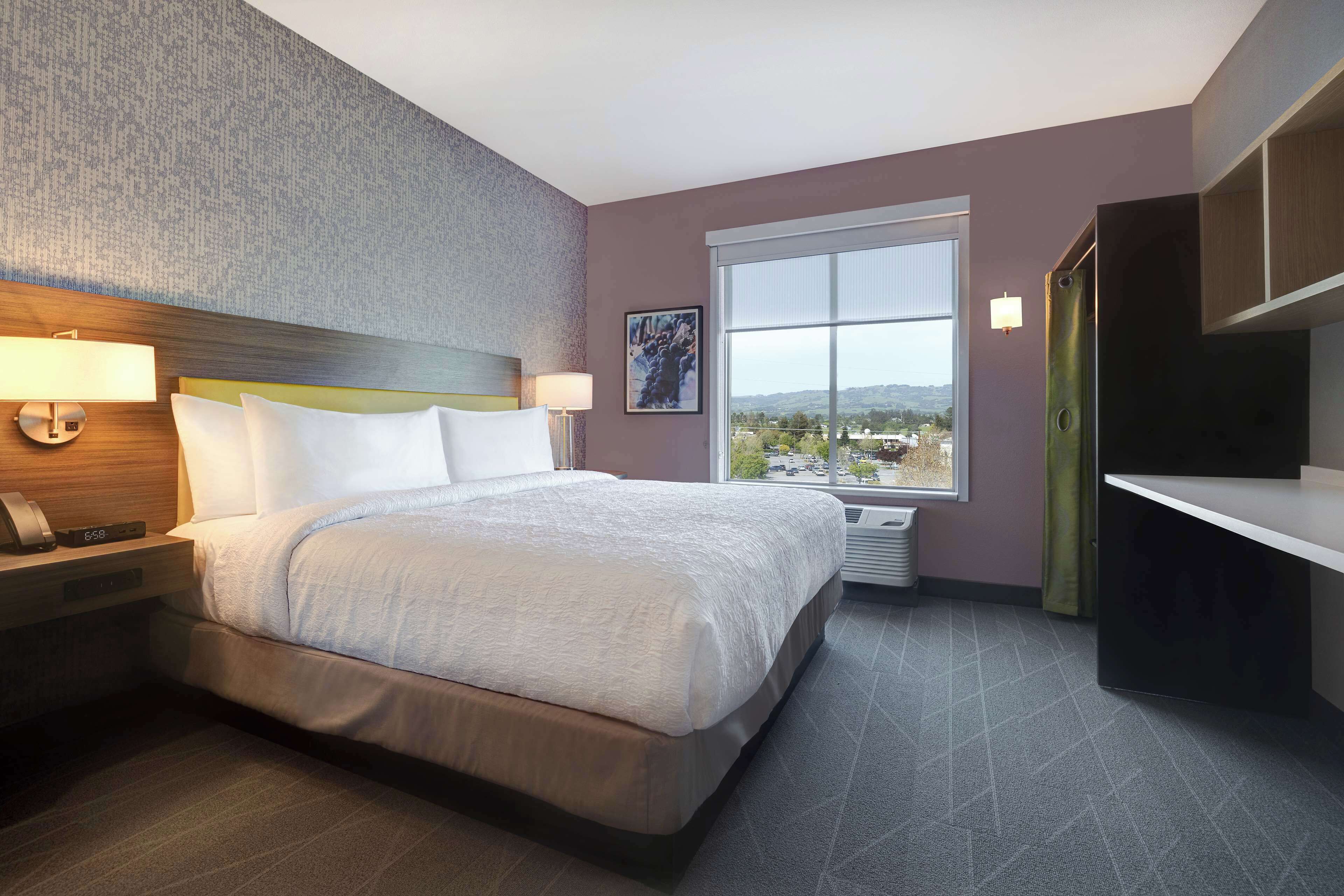 Una habitación de hotel moderna con una cama grande, lámparas de noche, un escritorio y una ventana con vista a la ciudad.