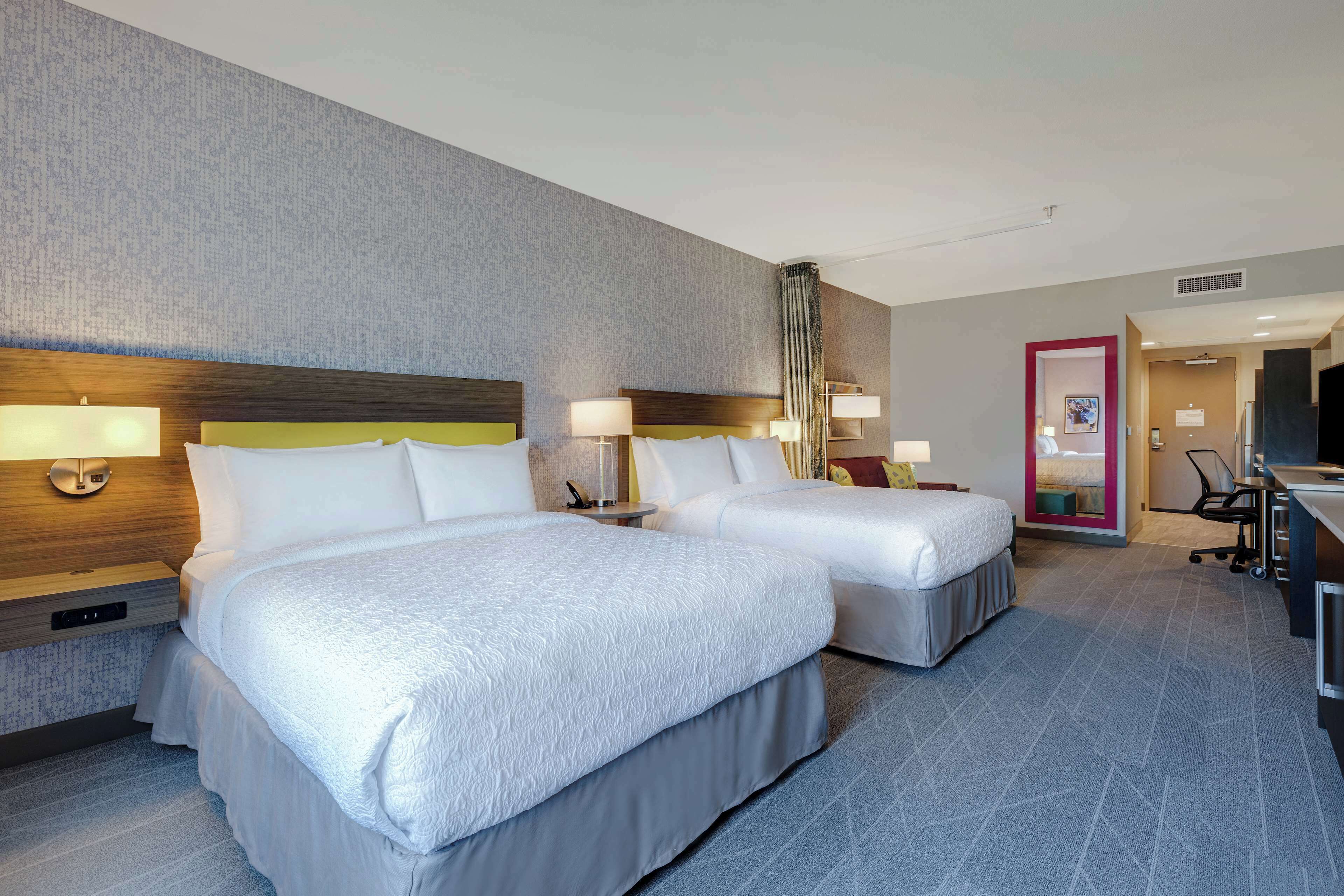 A hotel room with two beds, a desk, a chair, and a bathroom door.