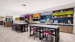 A modern restaurant with a clean, bright interior, featuring a counter with a menu, a seating area with tables and chairs, and a decorative wall with a 'Good Morning' sign.
