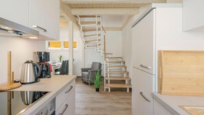 Una cocina moderna con estufa integrada, cafetera y comedor con mesa y sillas. Una escalera conduce a un segundo piso.