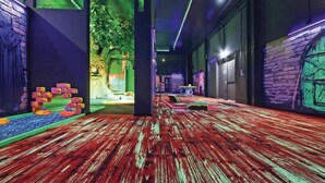 A hallway with a red wooden floor, a green wall with a tree mural, and a brick wall with a green door. - Ferienhausdorf Thale (Thale)