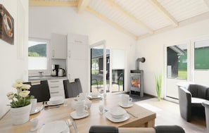 A modern kitchen with white cabinets, a dining area with a table set for four, and a wood-burning stove. - Ferienhausdorf Thale (Thale)