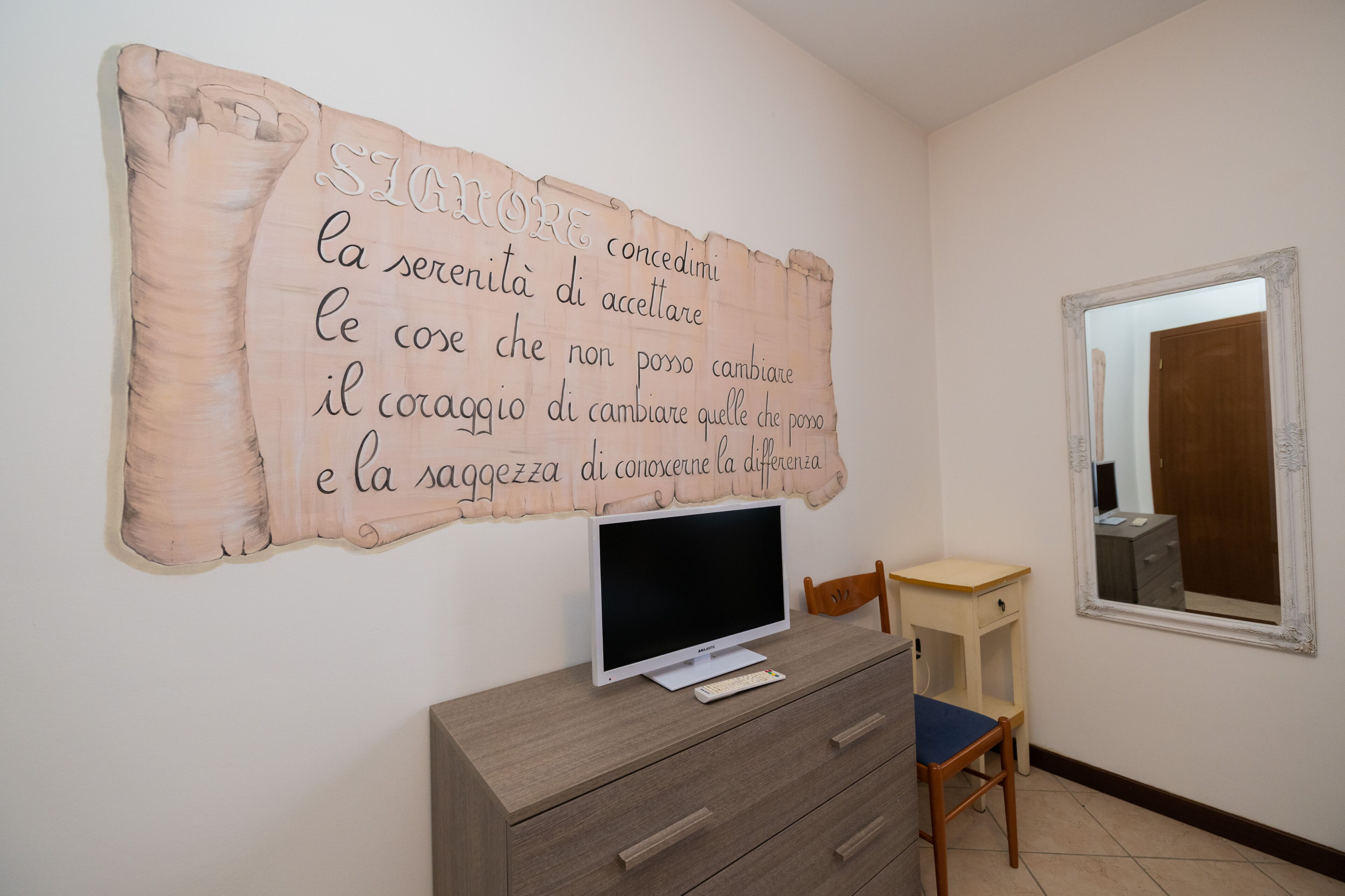Une pièce décorée d’un grand élément mural, avec un téléviseur à écran plat posé sur une commode en bois, une chaise et un miroir accroché au mur.