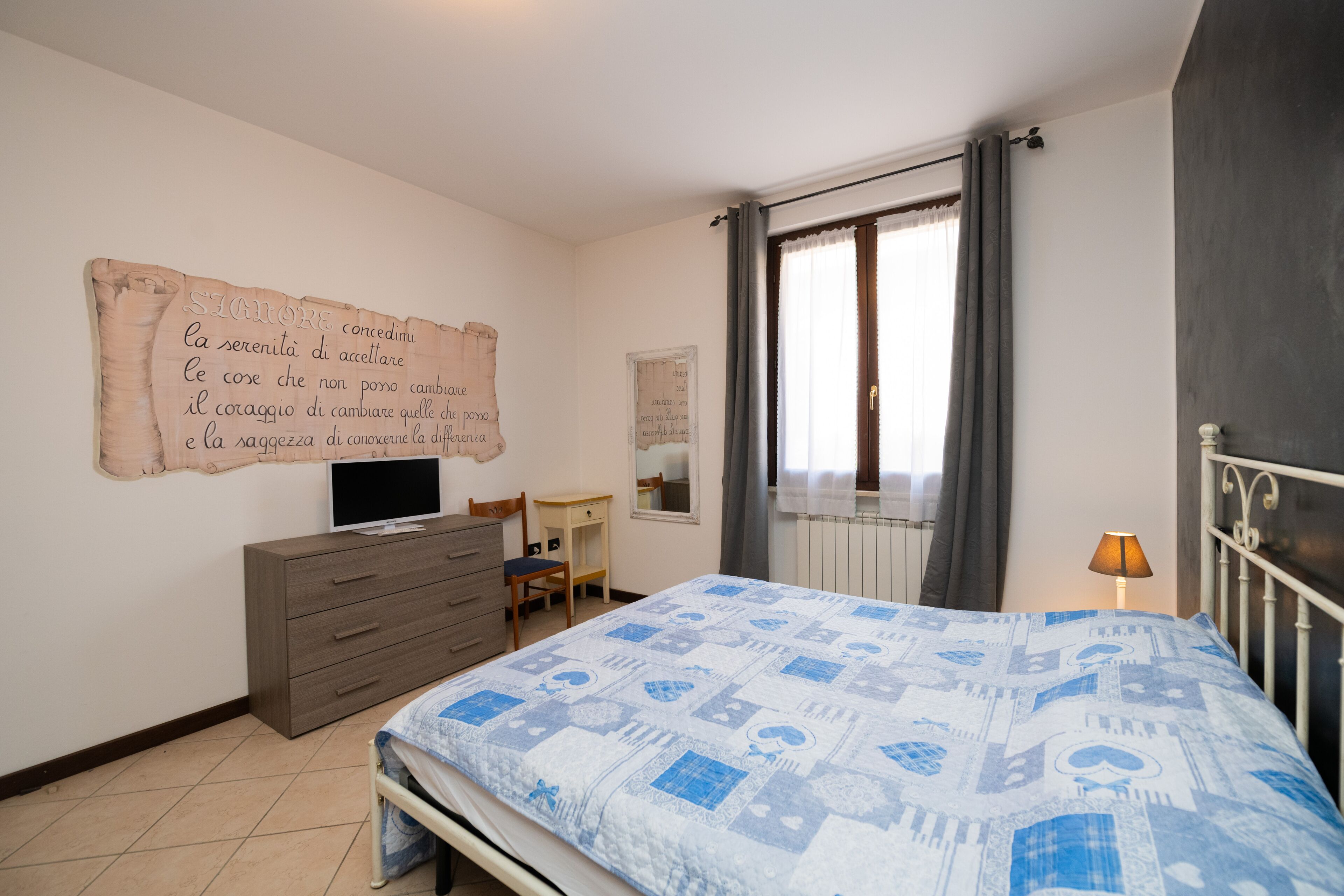 A bedroom with a bed, a dresser, a TV, a chair, and a window with curtains.