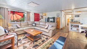A cozy living room with a sectional sofa, a wooden coffee table, and a kitchen area with a microwave and shelves. - Cabin in the forest, close to Bass Lake & Yosemite, mountain views & deck (Oakhurst)