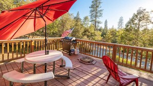 A wooden deck with a table and chairs, an umbrella, and a grill. - Cabin in the forest, close to Bass Lake & Yosemite, mountain views & deck (Oakhurst)