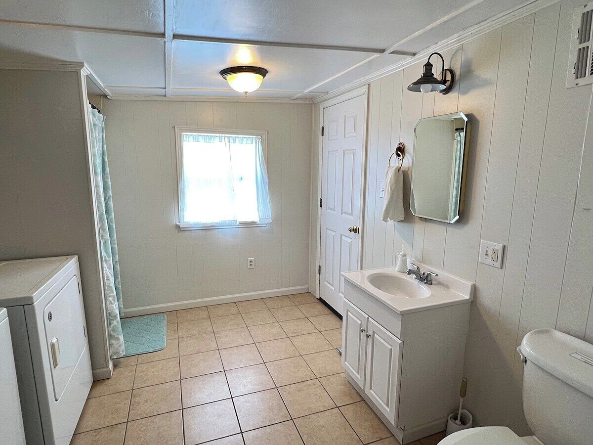 A bathroom with a toilet, sink, mirror, and window.