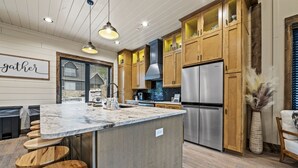 Une cuisine moderne avec des meubles en bois, un réfrigérateur en acier inoxydable et un îlot en marbre agrémenté de tabourets de bar.