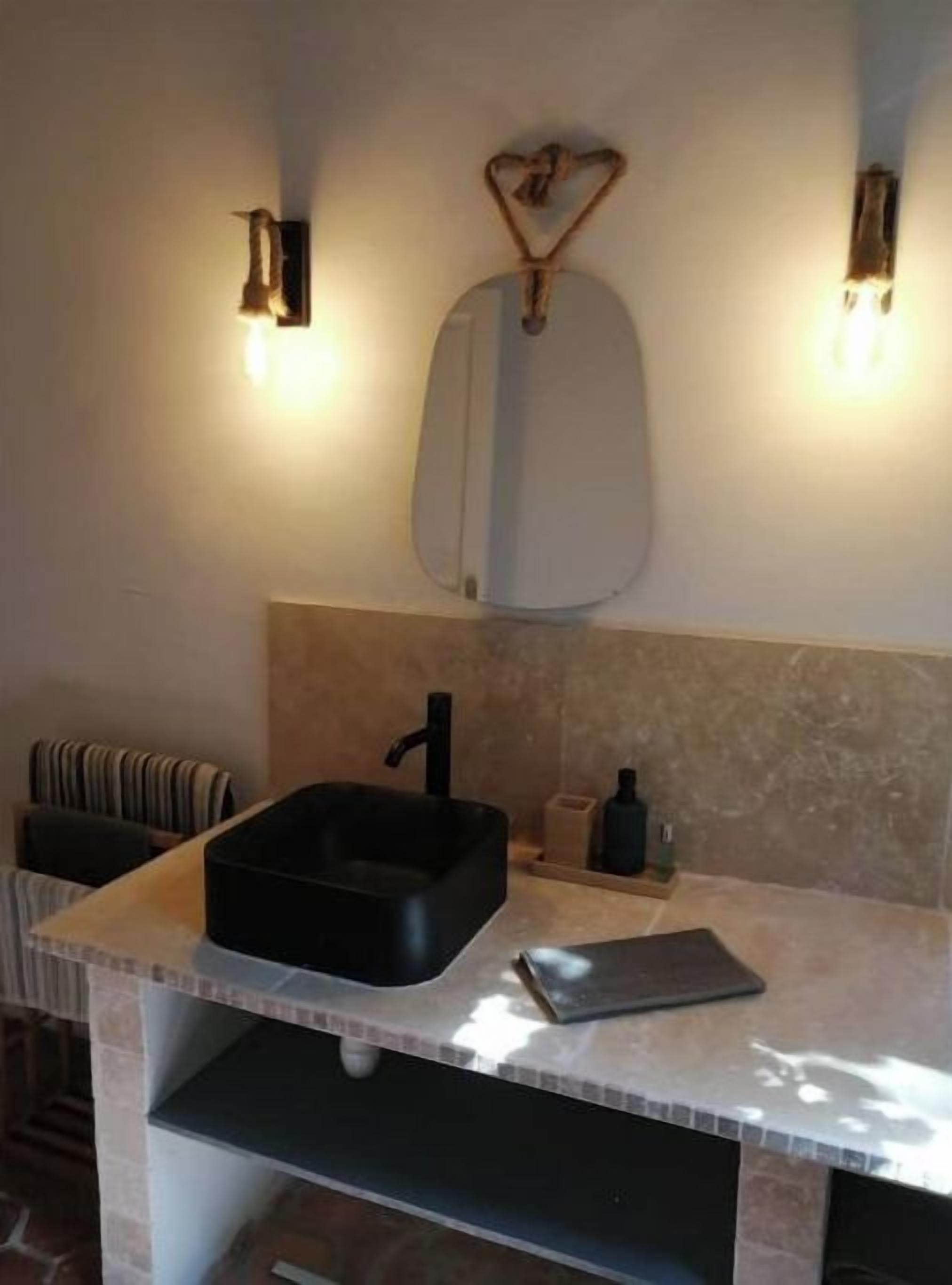 Une salle de bain avec un lavabo noir, un miroir et deux appliques murales.