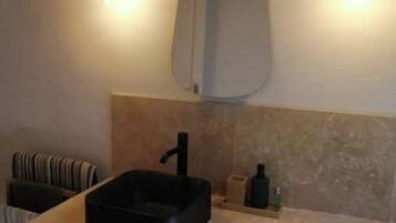 Une salle de bain avec un lavabo noir, un miroir et deux appliques murales.