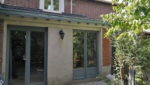 A brick house with a covered patio, large glass doors, and a small garden. - Nice, friendly house near Paris (Argenteuil)