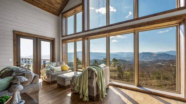 Ein geräumiges Wohnzimmer mit großen Fenstern und Blick auf die Berge, Holzböden und bequemen Sitzgelegenheiten.