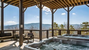 Eine Holzterrasse mit Whirlpools und Sitzgelegenheiten mit Blick auf eine gebirgige Landschaft.
